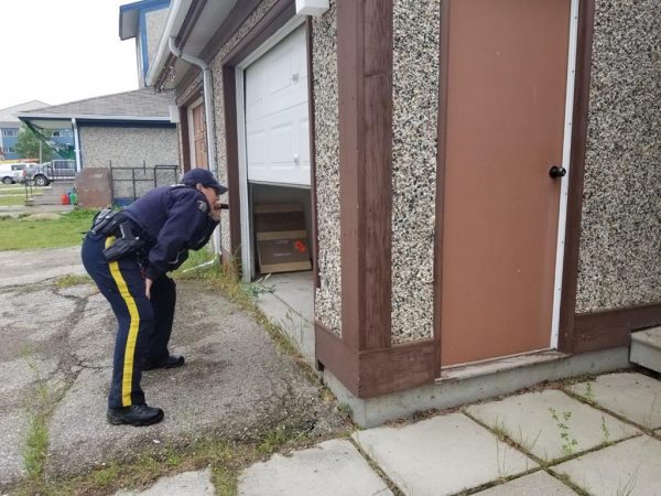 An RCMP officer shines a light into an open garage at a home in the Gillam, MB., area in July 27, 2019, police image published to social media. (HO-Twitter, Royal Canadian Mounted Police, @rcmpmb/The Canadian Press)