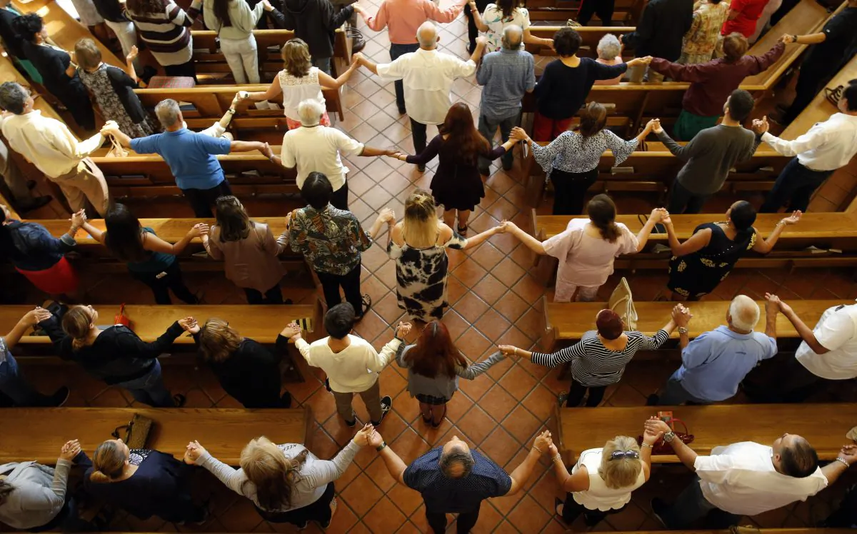 Churchgoers hold hands as they sing during a morning service at St. Pius X Catholic Church in El Paso, Texas, on Aug. 4, 2019. (Vernon Bryant/The Dallas Morning News via AP)
