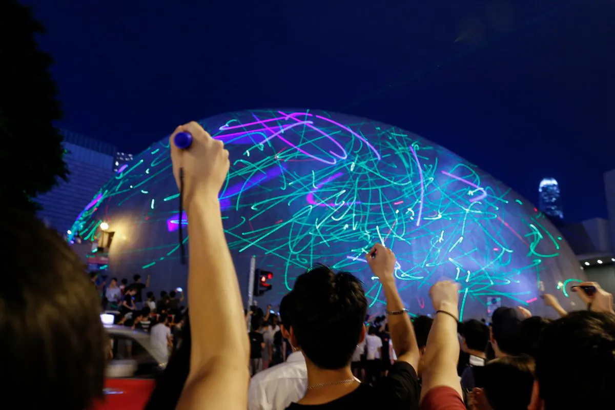 People watch the dots of laser pointers move across the facade of the Hong Kong Space Museum during a flashmob staged to denounce the authorities' claim that laser pointers were offensive weapons in Hong Kong, China on Aug. 7, 2019. (Thomas Peter/Reuters)