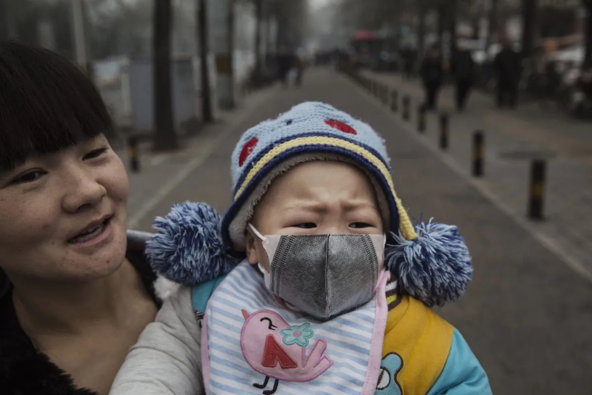 A Chinese girl wears a mask as she is held by her mother outside a local hospital during a day of heavy smog in Beijing on Dec. 8, 2015. (Kevin Frayer/Getty Images)