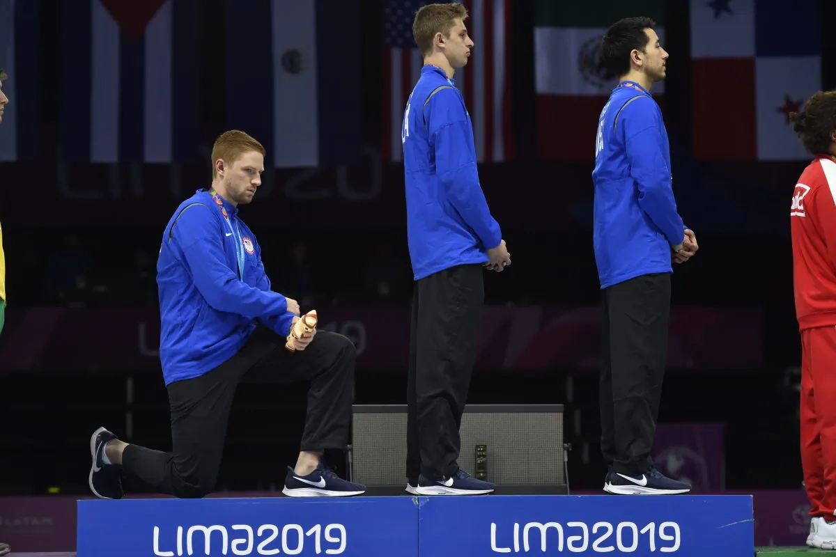Race Imboden, left, kneels next to Nick Itkin, and Gerek Meinhardt during the national anthem at the Men's Foil Team medal ceremony during the Pan American Games Lima 2019 on Aug. 9, 2019. (Jose Sotomayor-Lima 2019/AFP/Getty Images)