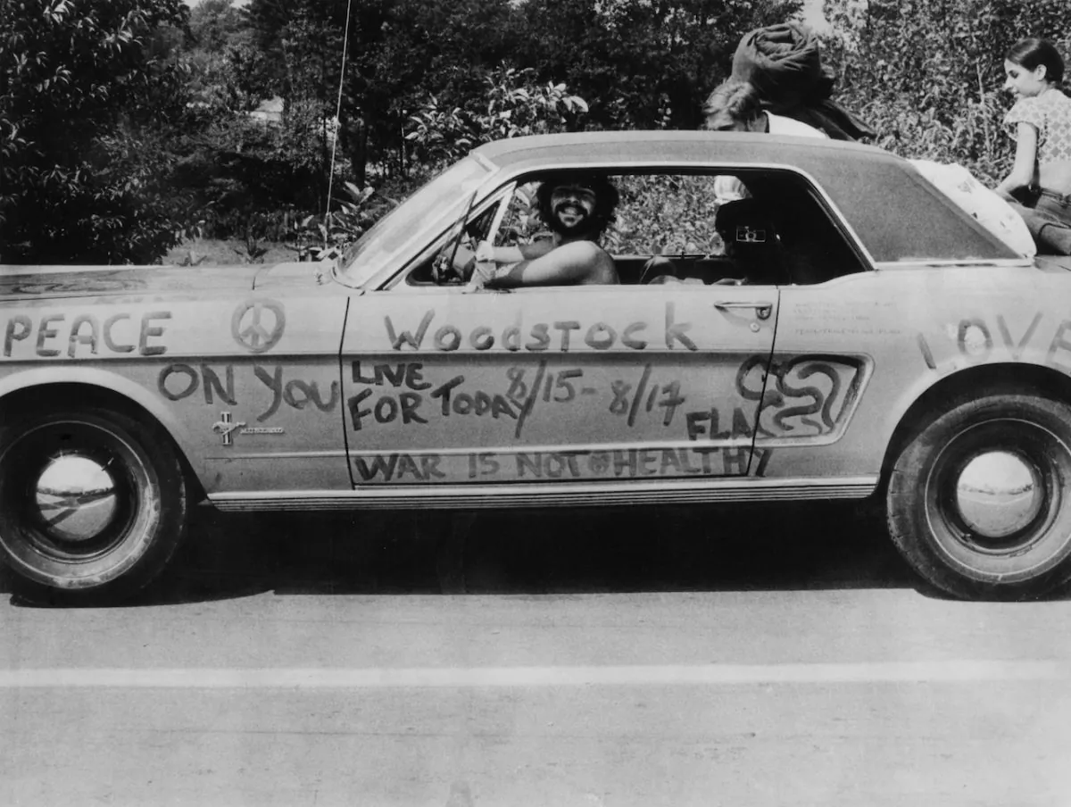 A music fan at Woodstock pop festival in his car covered in anti-war slogans for love and peace. (Photo by Three Lions/Getty Images)