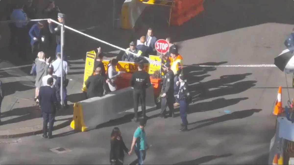 People walk past security officers standing around a barricaded area, following reports of a stabbing incident in the central business district of Sydney, Australia on Aug. 13, 2019, in this still image from video obtained via social media. (Twitter @THEBORINGGIT via Reuters)