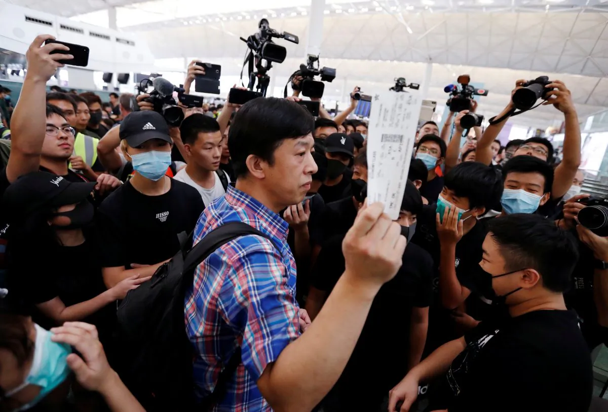 A passenger walks past anti-government protesters as he tries to enter the security gate during a demonstration at Hong Kong Airport, China on Aug. 13, 2019. (Issei Kato/Reuters)