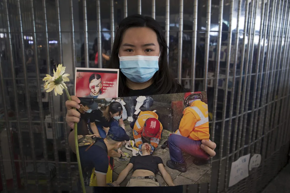 A woman holds a flower and posters showing people injured by police as protesters stage a sit-in rally at he Hong Kong International Airport in Hong Kong, on Aug. 13, 2019. (AP Photo/Vincent Thian)