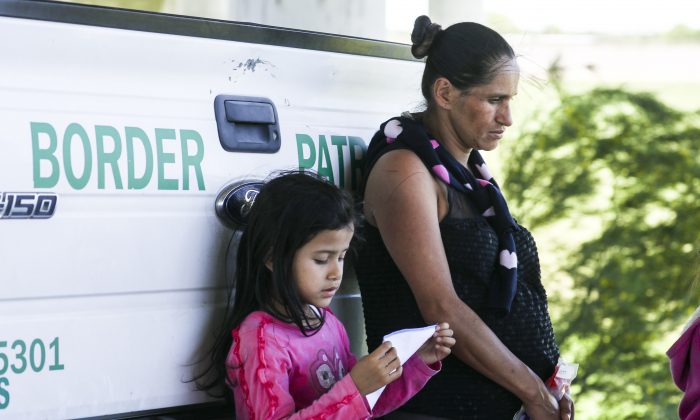 A heavily pregnant woman and a girl lean against a Border Patrol truck after being apprehended for illegally crossing the U.S. border over the Rio Grande from Mexico near McAllen, Texas, on April 18, 2019. (Charlotte Cuthbertson/The Epoch Times)