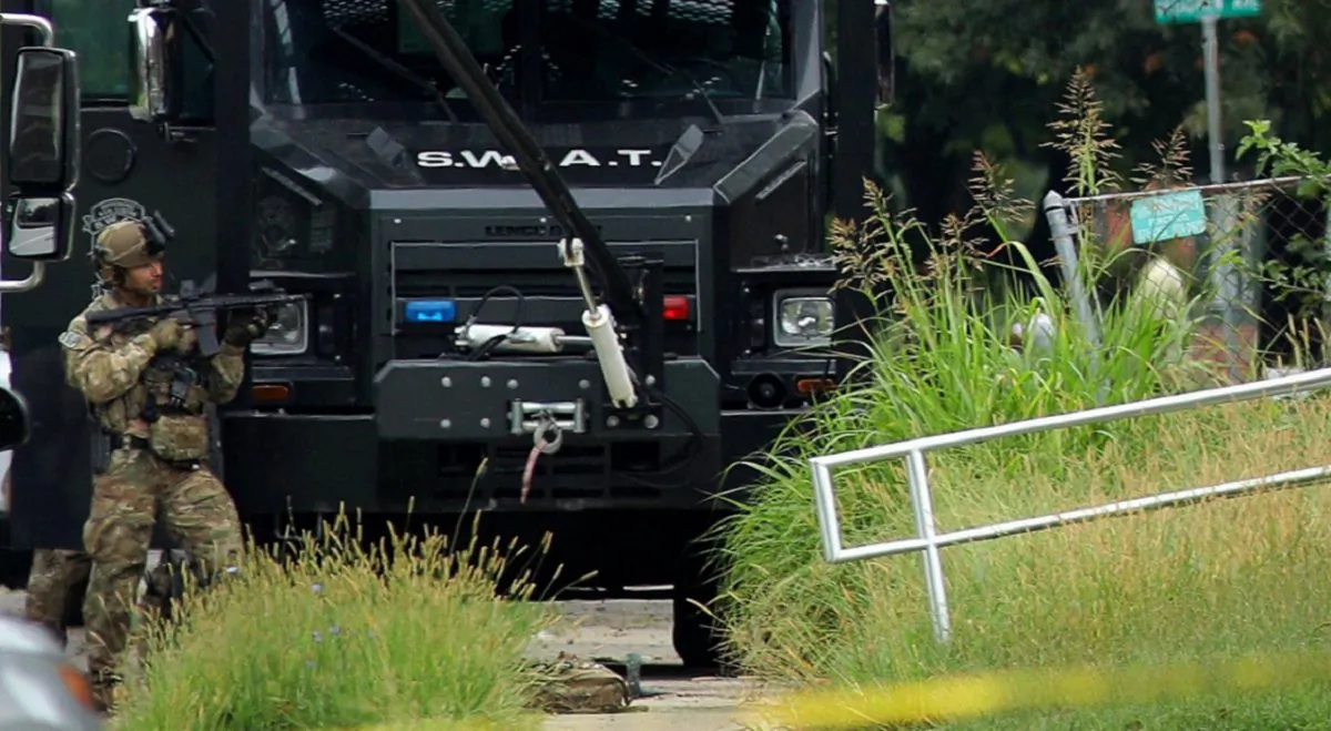 A police officer in tactical gear stands positioned near an Illinois State Police S.W.A.T. vehicle outside a building on 42nd Street near Van Buren Avenue,in East St. Louis, Ill., after a state trooper was shot while serving a warrant at the address on Aug 23, 2019. (Christian Gooden/St. Louis Post-Dispatch via AP)