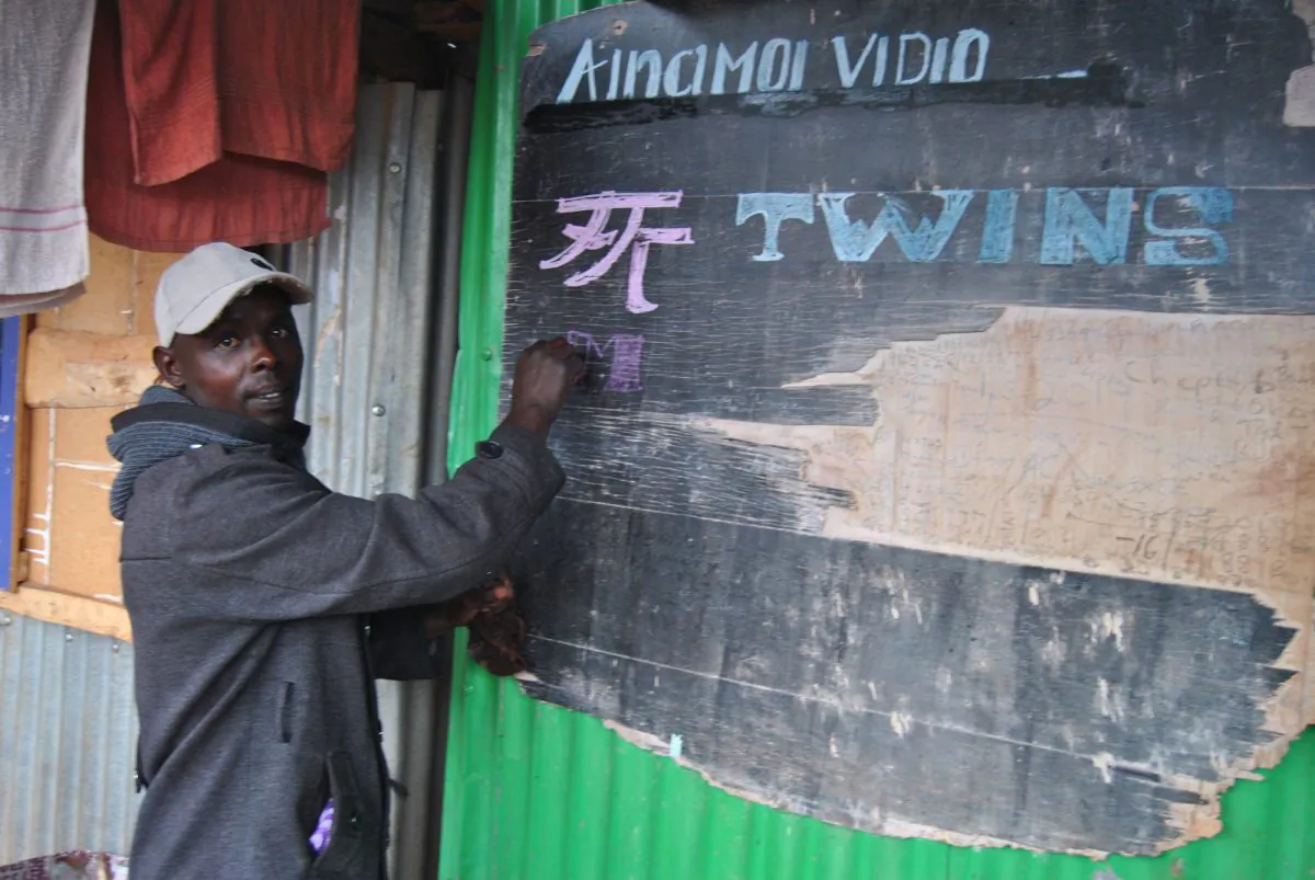 Leonard Biegon writes the name of the current Chinese movie showing at his video store at the Ainamoi shopping center, Kenya, on Aug. 24, 2019. (Dominic Kirui for The Epoch Times)
