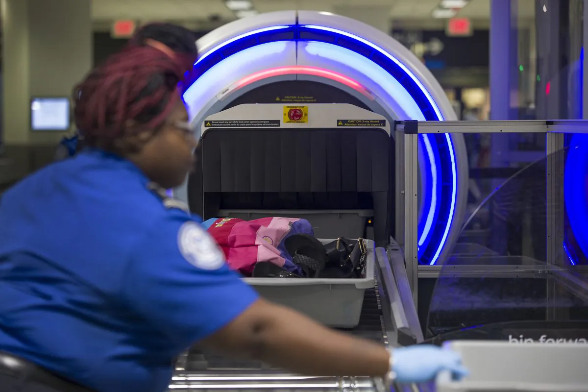 A Transportation Security Administration (TSA) agent helps travelers place their bags through the 3-D scanner at the Miami International Airport on May 21, 2019. (Joe Raedle/Getty Images)
