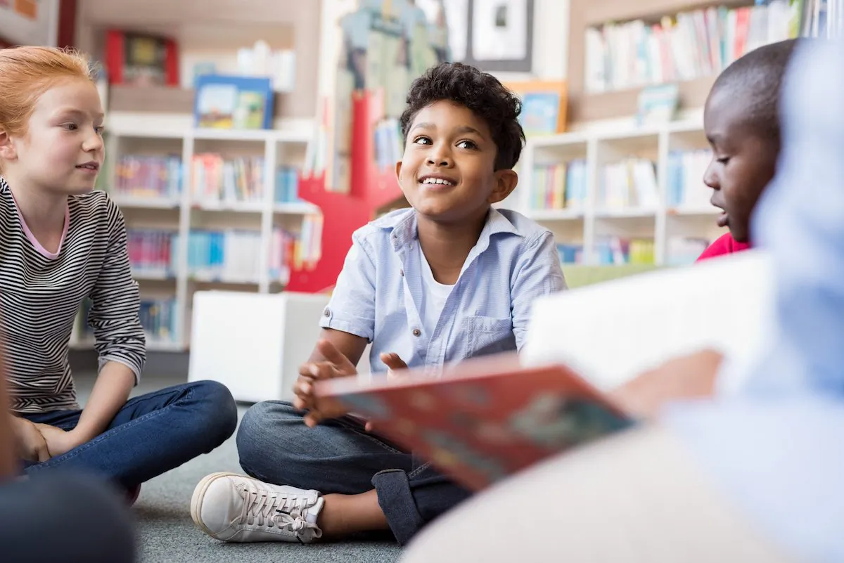 Multiethnic group of kids sitting on floor in circle around the teacher and listening a story. (Shutterstock)