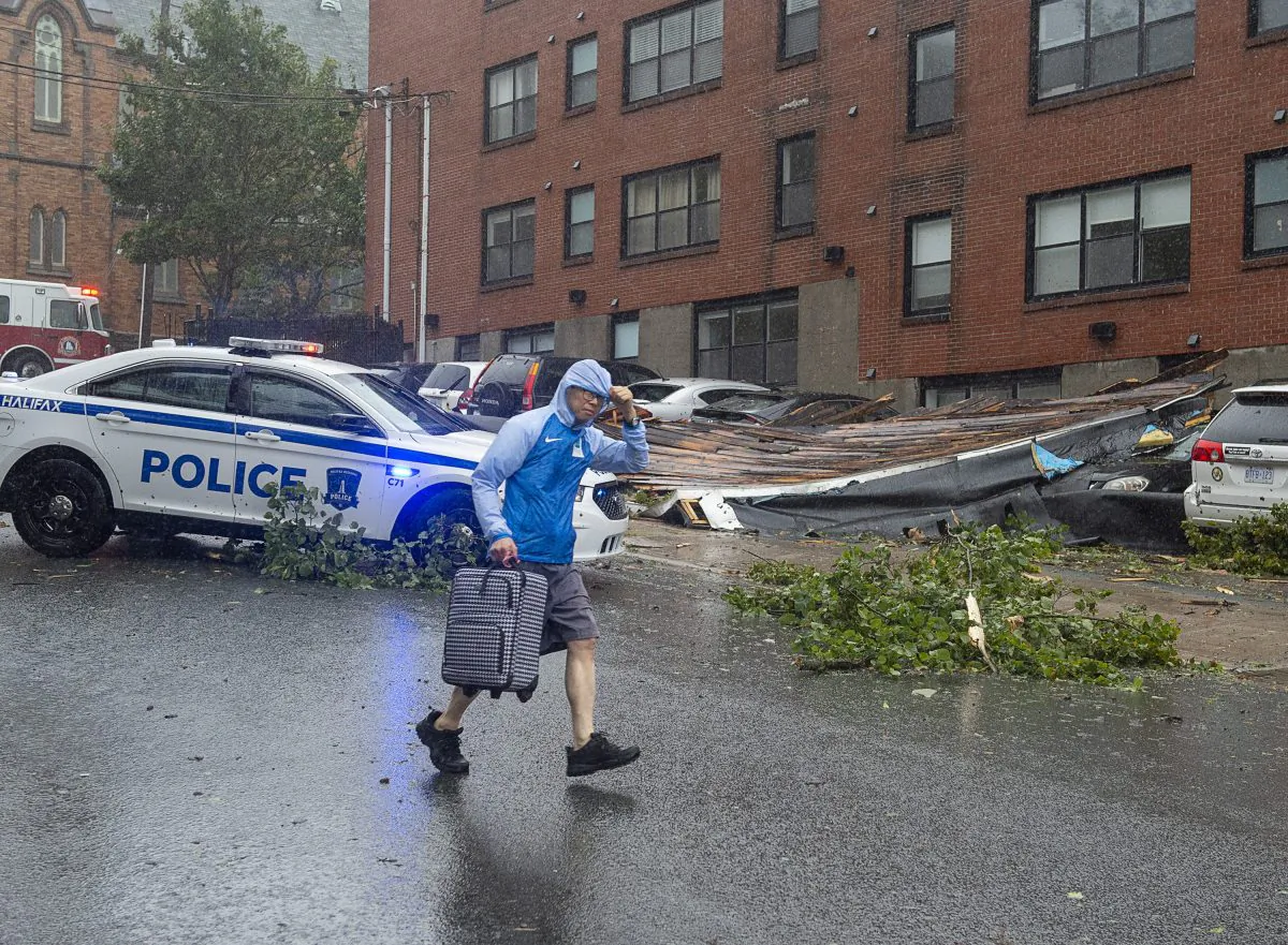 A man heads past part of an apartment roof that landed on several cars in Halifax as hurricane Dorian approaches on Sept. 7, 2019. (The Canadian Press/Andrew Vaughan)