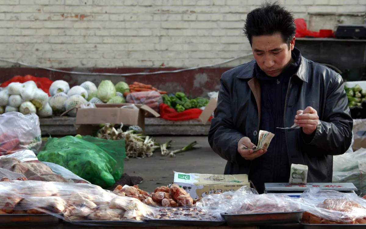 Fruit and vegetables can be seen behind a man selling pork as he checks his money at a small roadside market in central Beijing, China on March 1, 2011. (David Gray/Reuters)
