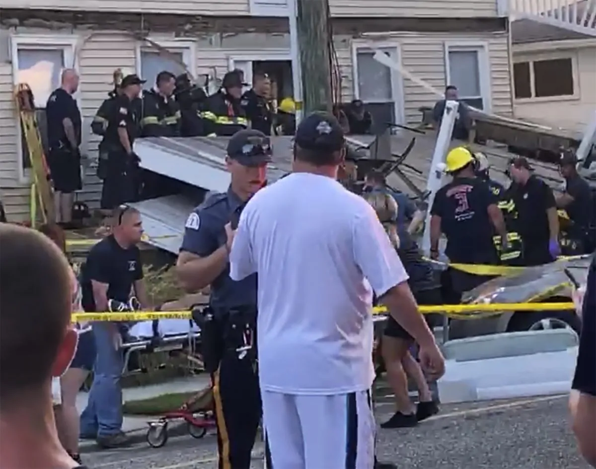 A first responder talks to an onlooker as others carry an injured person, while some others work the scene of a building structure damage, in the background, in Wildwood, N.J., on Sept. 14, 2019. (James Macheda via AP)