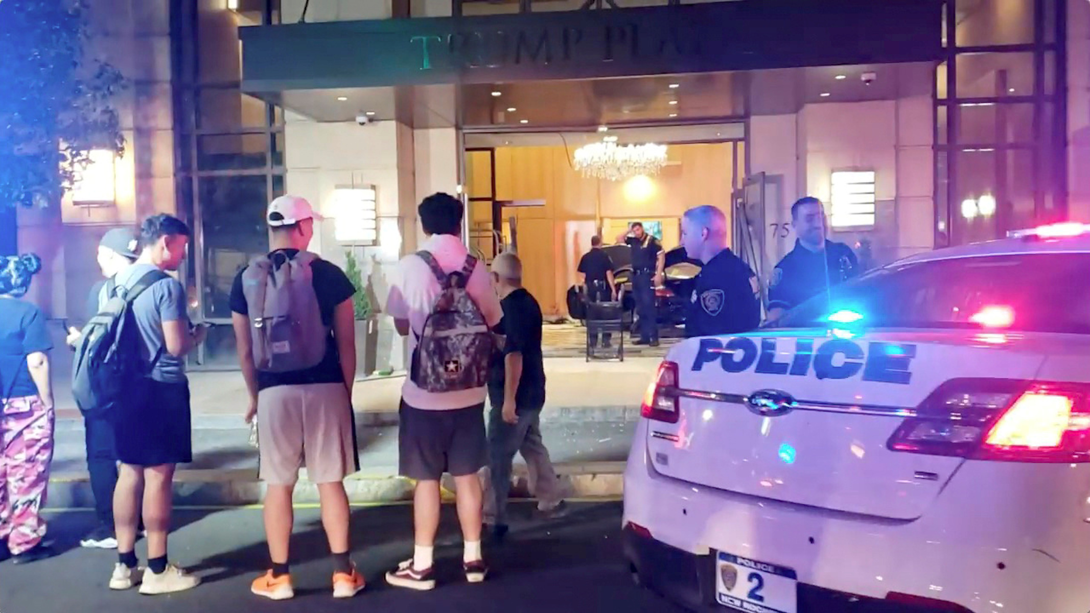 People and police officers stand outside Trump Plaza after a car crashed into the building's lobby in New Rochelle, New York