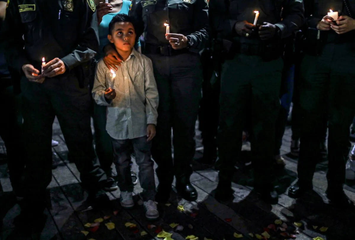 A boy holds a candle next to members of the national police during a tribute to the victims of a car bomb attack in Bogota, Colombia, near Medelin on Jan. 19, 2019. The government has accused the leftist group ELN of carrying out the bombing. (Joaquin Sarmiento     /AFP/Getty Images)