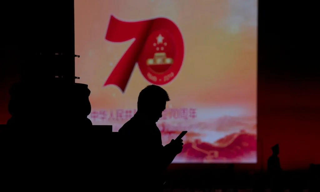 A man uses his mobile phone in front of a screen that shows a message about the 70th anniversary of the founding of the Chinese communist regime, in Beijing on Sept. 26, 2019. (Noel Celis/AFP/Getty Images)