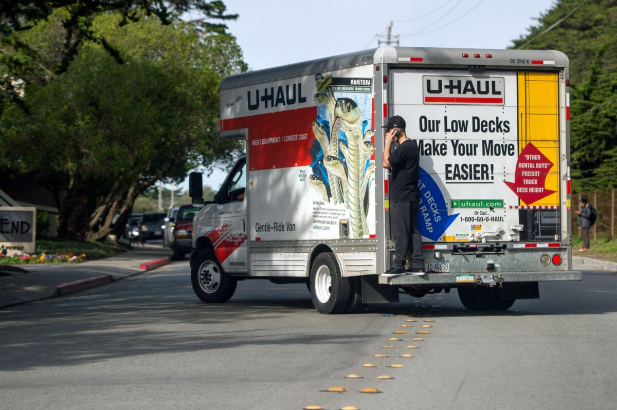 A man talks on his cell phone while riding on the back of a moving truck