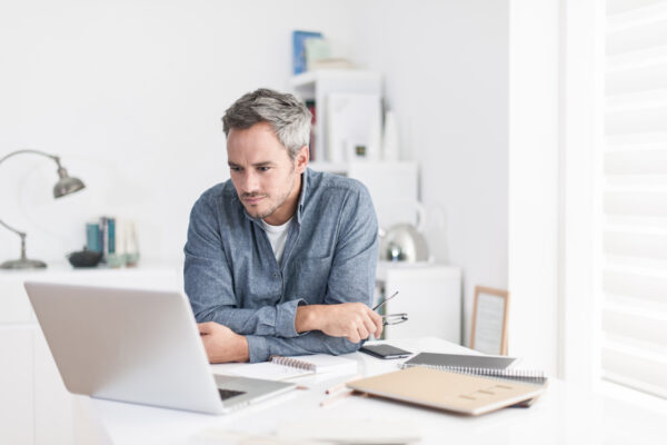 man is sitting at a white table looking at his laptop