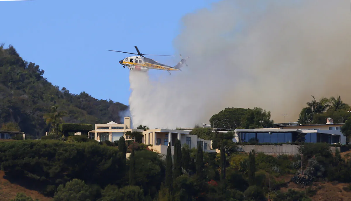 A helicopter makes a water drop as flames threaten homes on a ridgeline as a wildfire threatens homes in the Pacific Palisades area of Los Angeles on Oct. 21, 2019. (Reed Saxon/AP Photo)