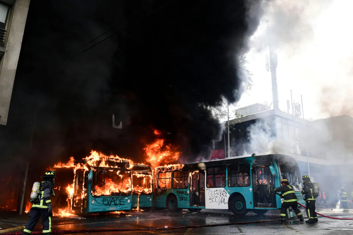 Chilean firefighters extinguish burning buses during clashes between protesters and the riot police in Santiago, on Oct. 19, 2019. (MARTIN BERNETTI/AFP via Getty Images)