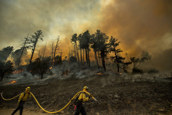 A hillside smolders as firefighters light backfires