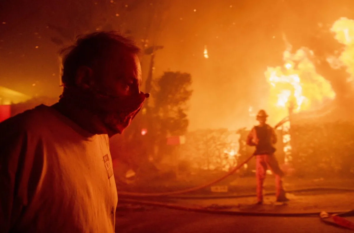 A man walks past a burning home during the Getty fire, Monday, Oct. 28, 2019, in Los Angeles, Calif. (AP Photo/ Christian Monterrosa)