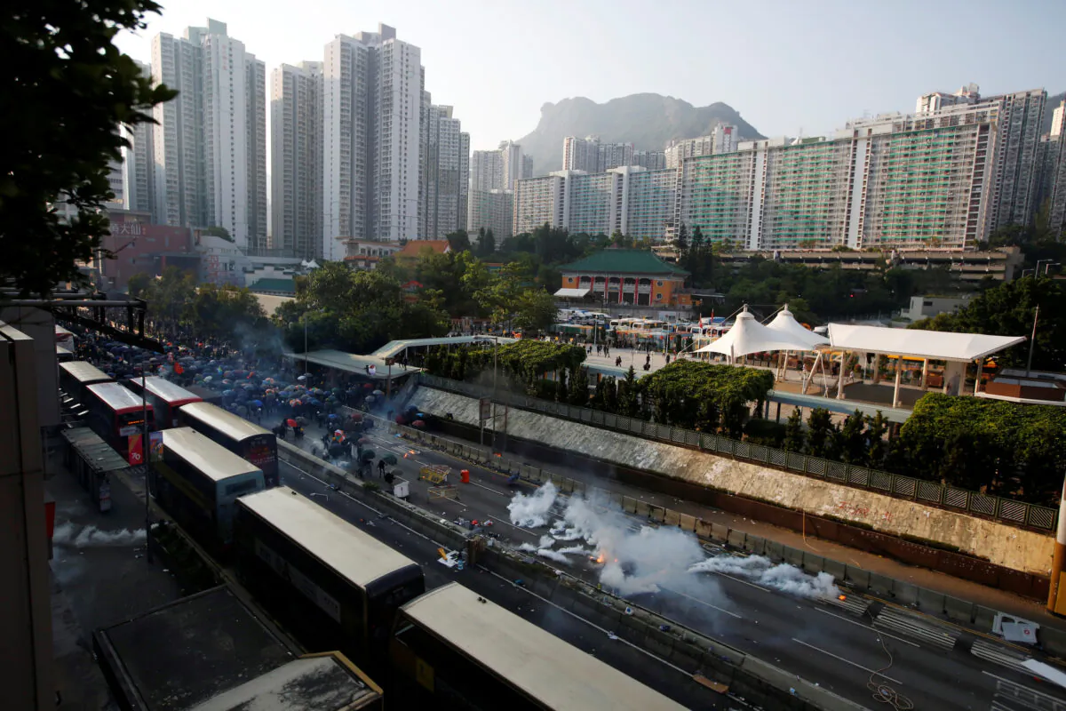 Hundreds of protesters huddle behind umbrellas on Lung Cheung Road in the Wong Tai Sin neighborhood as they face off riot police who are firing tear gas toward them, with Lion Rock in the background, in Hong Kong on Oct. 1, 2019. (James Pomfret/Reuters)