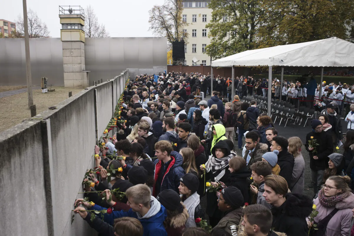 Young people stuck flowers in remains of the Berlin Wall during a commemoration ceremony to celebrate the 30th anniversary of the fall of the Berlin Wall at the Wall memorial site at Bernauer Strasse in Berlin, Nov. 9, 2019. (Markus Schreiber/AP Photo)