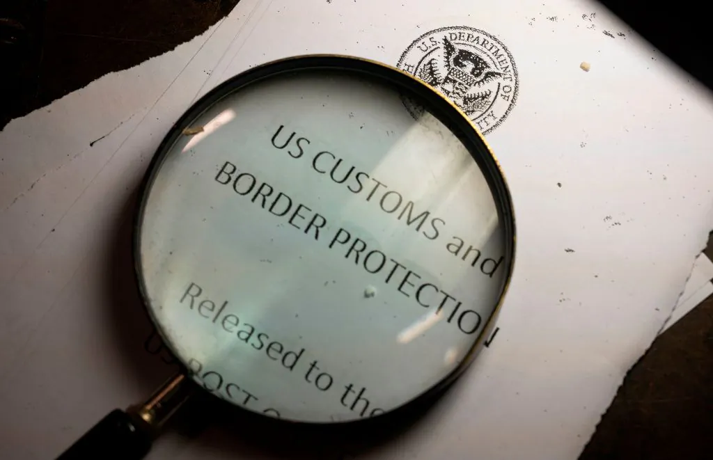 A magnifying glass is seen next to a logo of the Customs and Border Protection, Trade and Cargo Division at John F. Kennedy Airport's US Postal Service facility in New York on June 24, 2019. (Johannes Eisele /AFP via Getty Images)