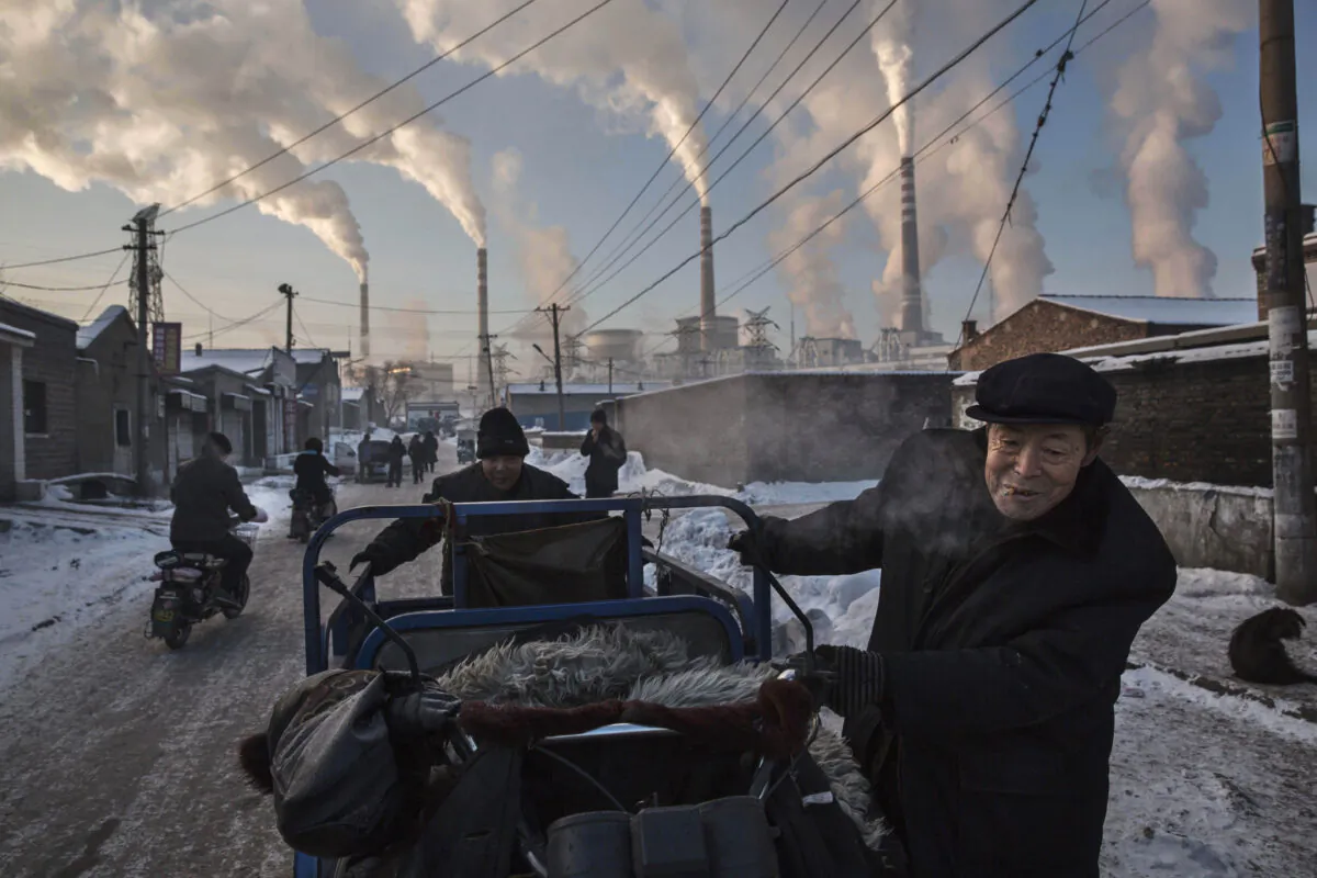 Smoke billows from stacks as Chinese men pull a tricycle in a neighborhood next to a coal fired power plant in Shanxi, China, on Nov. 26, 2015. (Kevin Frayer/Getty Images)