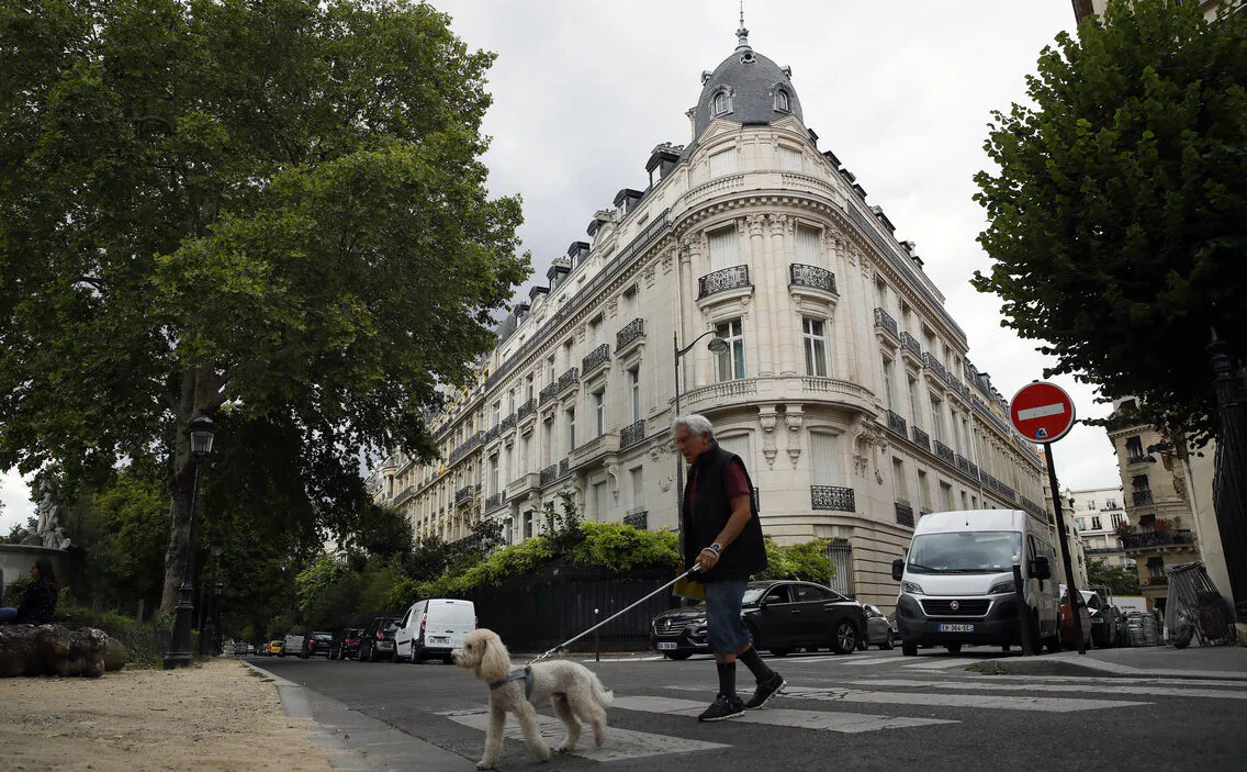 In this Aug.13, 2019 file photo, a man walks his dog next to an apartment building owned by Jeffrey Epstein in the 16th district in Paris on Aug. 13, 2019. (AP Photo/Francois Mori, File)