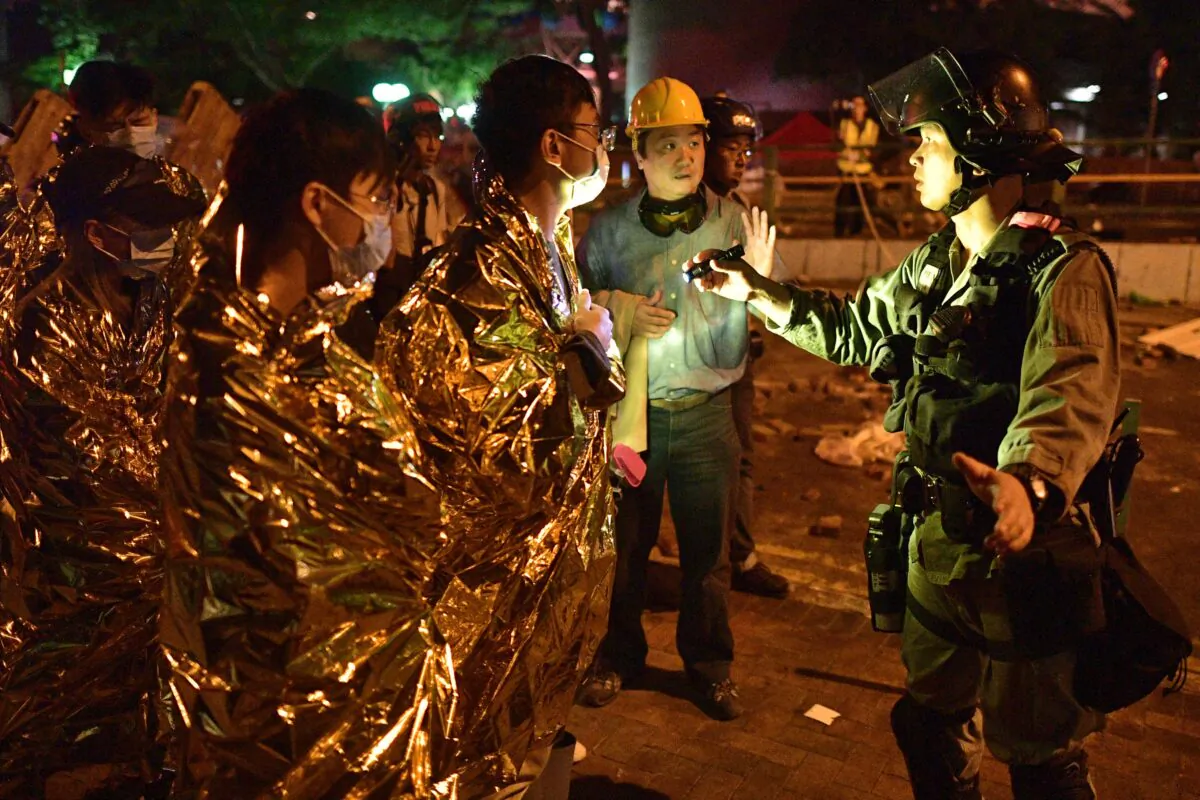 A policeman inspects the unwell and injured protesters wrapped in emergency thermal blankets, as they prepare to leave the campus of the Hong Kong Polytechnic University in the Hung Hom of Hong Kong on November 19, 2019. (NICOLAS ASFOURI/AFP via Getty Images)