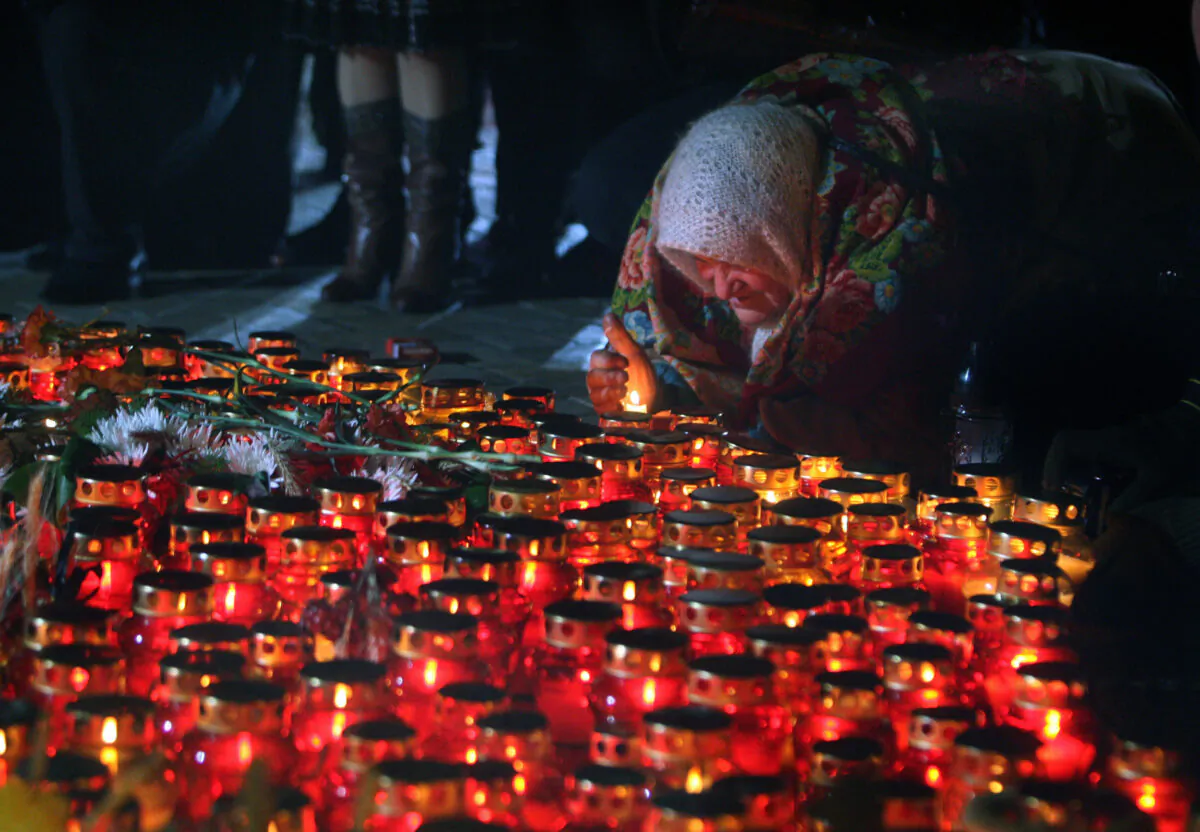 A woman kneels to light a candle during a mass memorial meeting at the Holodomor victims monument in Kiev, 24 Nov. 2007. (Sergei Supinsky/AFP via Getty Images)
