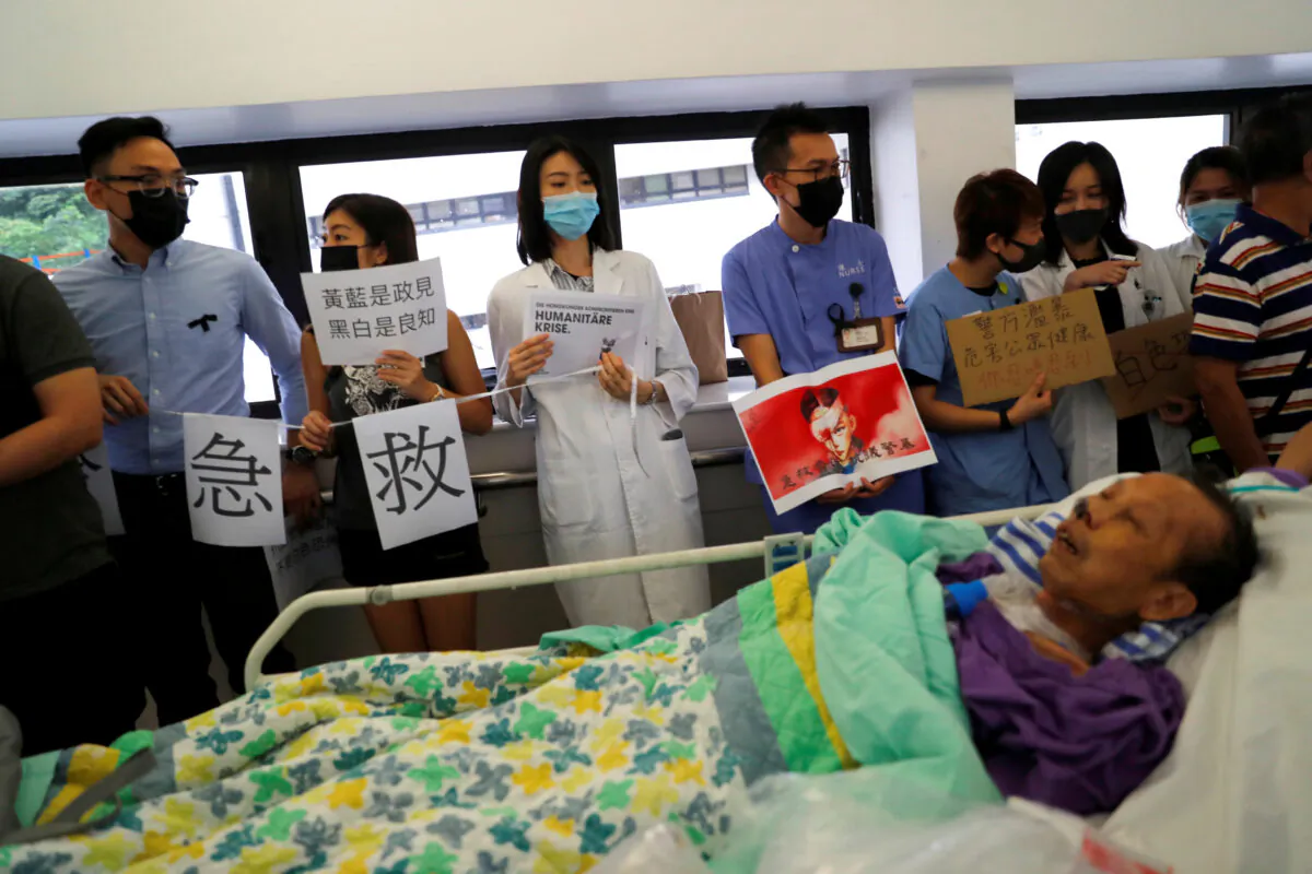 A patient is wheeled past as healthcare staff hold posters and participate in a human chain to protest against what they say is police brutality during the anti-extradition bill protests, at Queen Mary Hospital, in Hong Kong, China, on Sept. 2, 2019. (Anushree Fadnavis/Reuters)