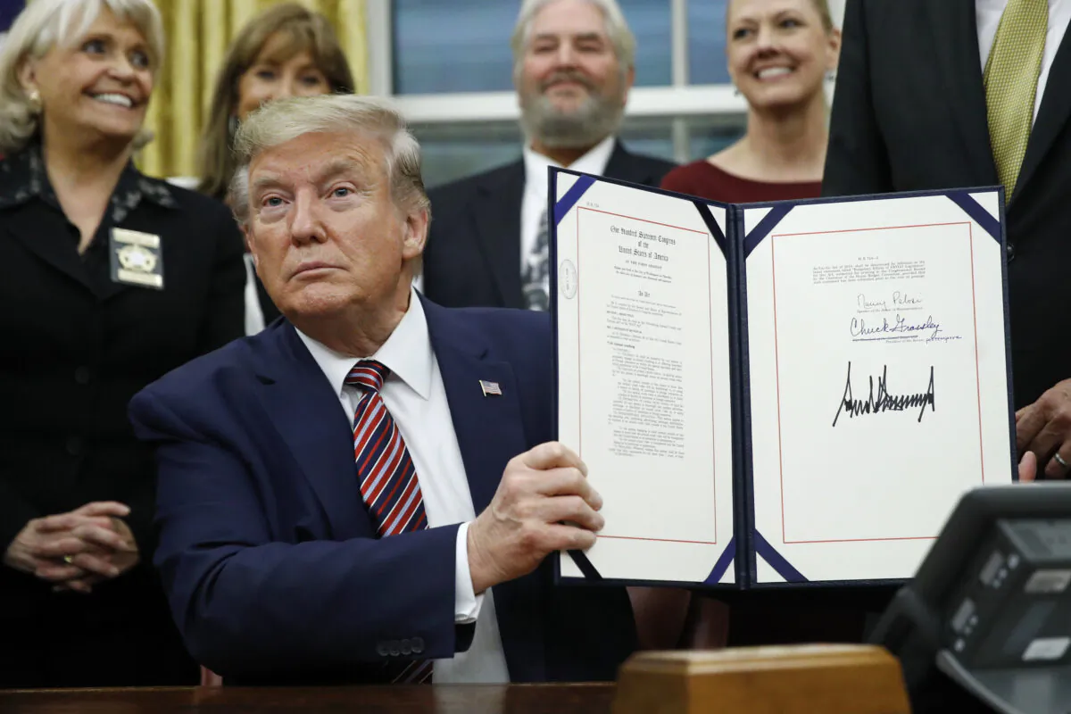 President Donald Trump displays the Preventing Animal Cruelty and Torture Act after signing it during a ceremony in the Oval Office of the White House, on Nov. 25, 2019. (Patrick Semansky/AP Photo)