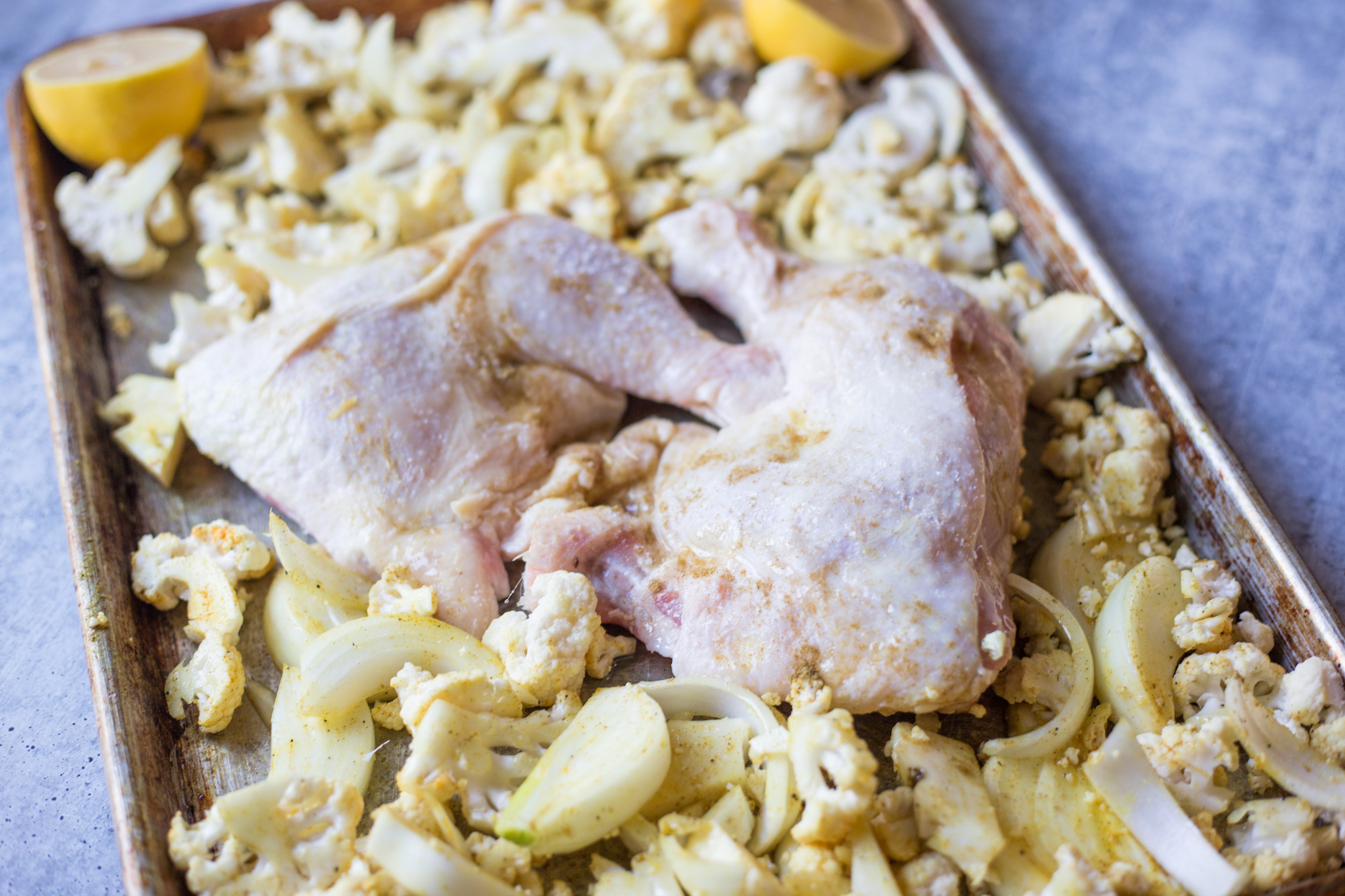 raw chicken thighs and cauliflower on a sheet pan