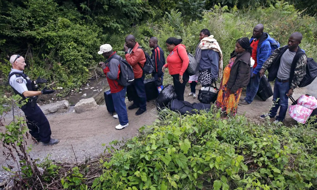 An RCMP officer standing in Saint-Bernard-de-Lacolle, Quebec, advises migrants who arrived from Champlain, N.Y., via Roxham Road that they are about to illegally cross into Canada and will be arrested, on Aug. 7, 2017. (AP Photo/Charles Krupa)