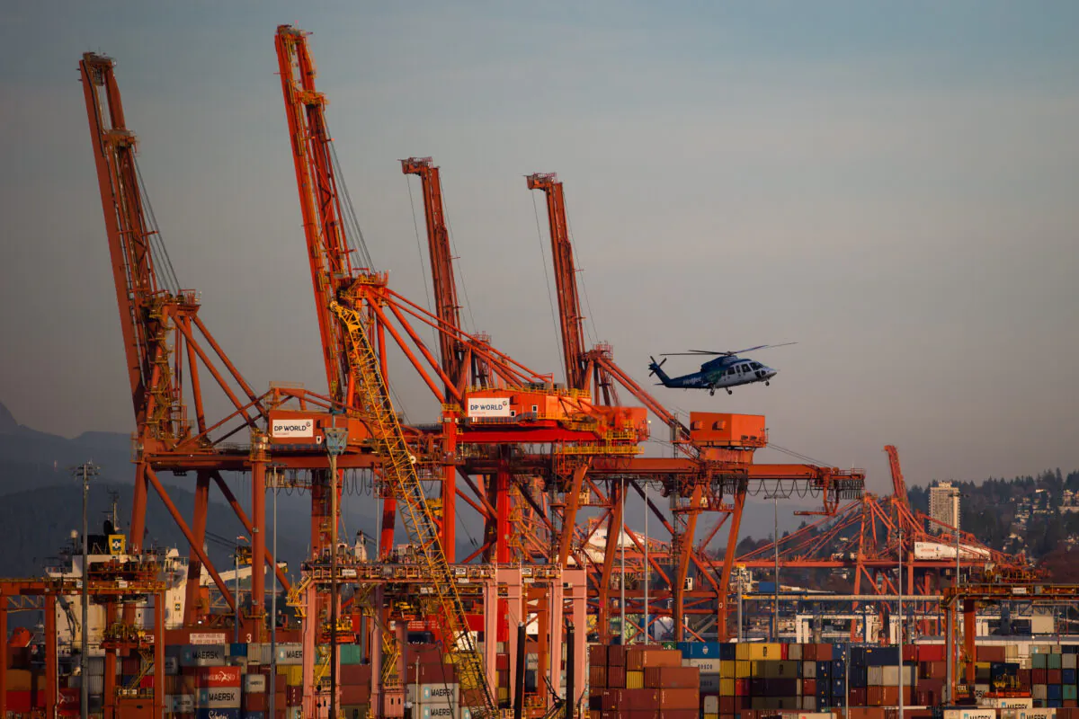 A helicopter flies past gantry cranes and cargo containers at a Port Metro Vancouver facility on Nov. 2, 2019. (Darryl Dyck/The Canadian Press)