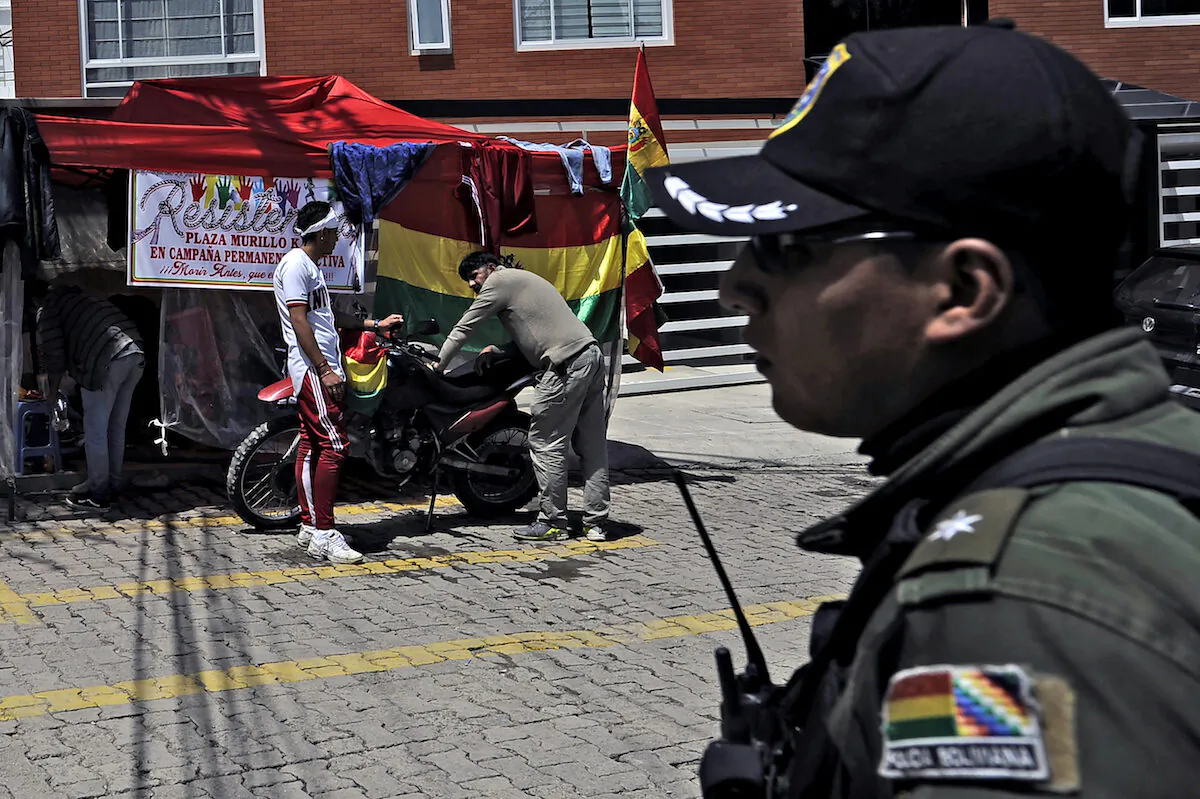 A policeman stands guard as opponents of Bolivian ex-president Evo Morales, exiled in Argentina, camp outside La Rinconada gated community, where the Mexican embassy is located, in La Paz on Dec. 30, 2019. (JORGE BERNAL/AFP via Getty Images)