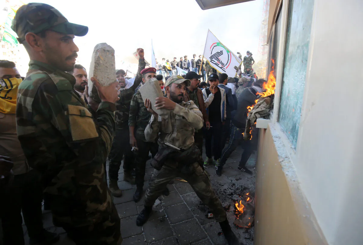 Members of the Hashed al-Shaabi, a group trained and armed by Iran, smash the bullet-proof glass of the U.S. embassy's windows in Baghdad with blocks of cement after breaching the outer wall of the diplomatic mission on Dec. 31, 2019. (Ahmad Al-Rubaye/AFP via Getty Images)