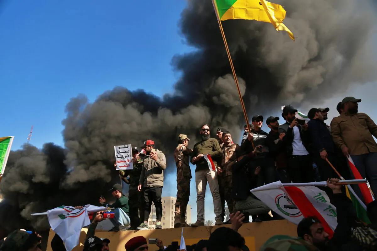 Attackers waving the Kataib Hezbollah terrorist group flag burn property in front of the U.S. embassy compound, in Baghdad, Iraq on Dec. 31, 2019. (Khalid Mohammed/AP)