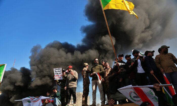 Attackers waving the Kataib Hezbollah terrorist group flag burn property in front of the U.S. embassy compound, in Baghdad, Iraq on Dec. 31, 2019. (Khalid Mohammed/AP)