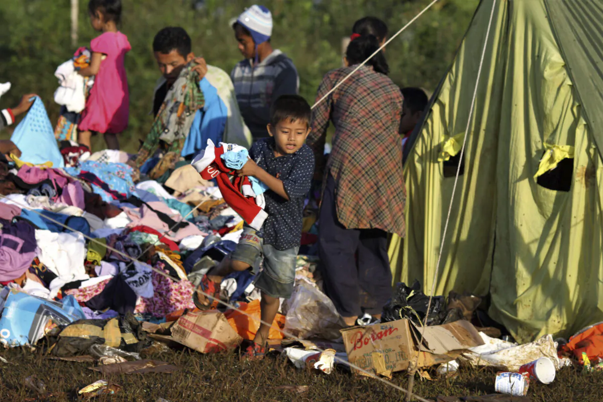 A young boy holds clothings he picked from a pile of relief goods at a temporary shelter for people who are affected by landslide, in Bogor, West Java, Indonesia on Jan. 5, 2020. (Rangga/AP)