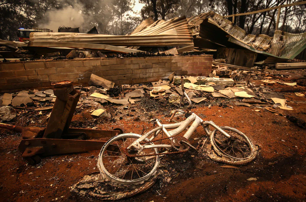 A burnt bicycle lies on the ground in front of a house recently destroyed by bushfires. (Photo by David Gray/Getty Images)
