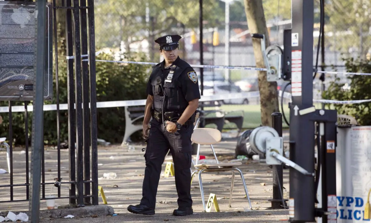 A police officer walks by yellow evidence markers at a playground after a shooting in the Brownsville neighborhood in Brooklyn, NYC, on July 28, 2019.  Mark Lennihan/AP Photo