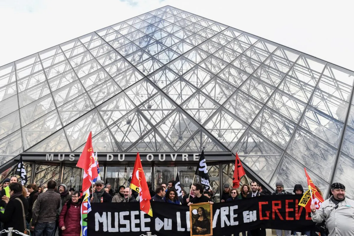 Employees and members of French trade unions hold flags and a banner reading "Musee du Louvre on strike" in front of the Louvre pyramid at the entrance of Louvre museum, in Paris, France, on Jan. 17, 2019. (Alain Jocard/AFP via Getty Images)