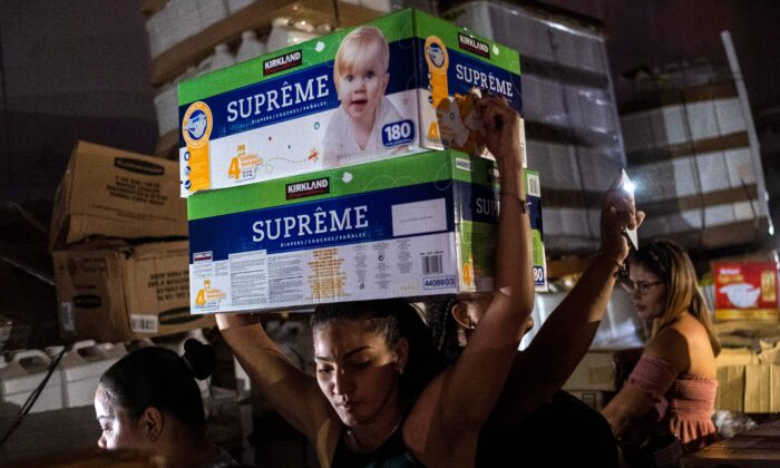 A woman carries boxes of baby diapers from warehouse filled with supplies, including thousands of cases of water, believed to have been from when Hurricane Maria struck the island in 2017 in Ponce, Puerto Rico, on Jan. 18, 2020. (Ricardo Arduengo/AFP via Getty Images)