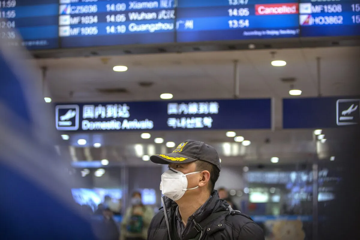 A traveler wears a face mask beneath an information display showing a canceled flight from Wuhan at Beijing Capital International Airport in Beijing on Jan. 23, 2020. (Mark Schiefelbein/AP Photo)