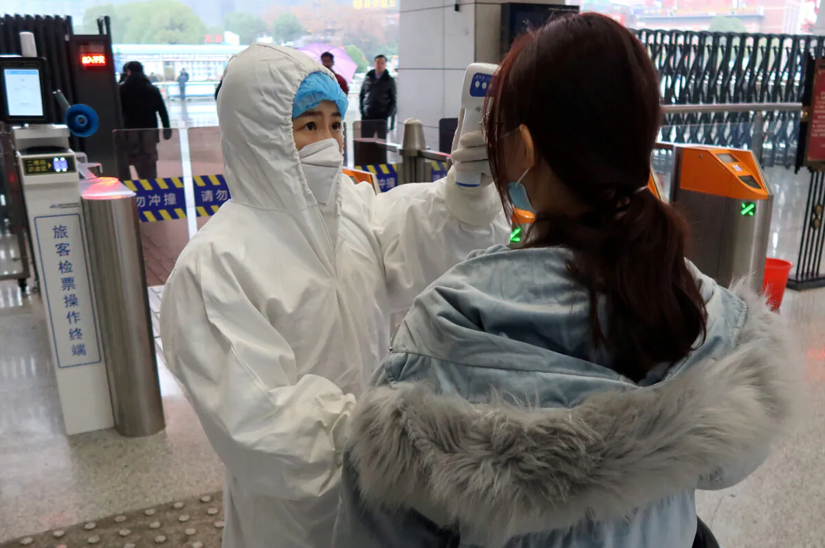 A worker in a protective suit checks the temperature of a passenger arriving at the Xianning North Station on the eve of the Chinese Lunar New Year celebrations, in Xianning city, Hubei Province, China, on Jan. 24, 2020. (Martin Pollard/Reuters)