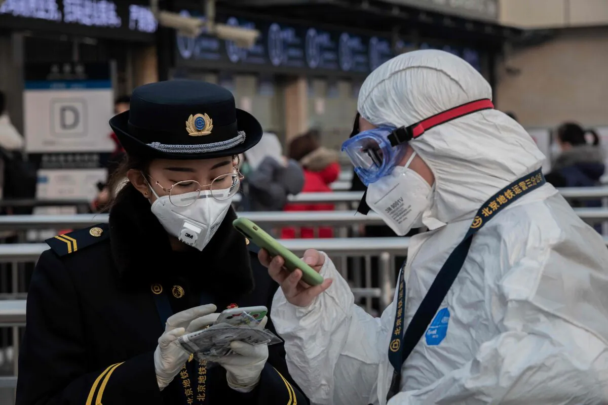 A security personnel wearing protective clothing to help stop the spread of a deadly virus that began in Wuhan, talks with a subway staff (L) wearing a mask at a subway station entrance in Beijing on Jan. 27, 2020. (Nicolas Asfouri/AFP via Getty Images)